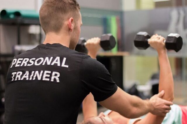 Entrenador personal ayudando a una persona entrenando en un gimnasio con pesas.